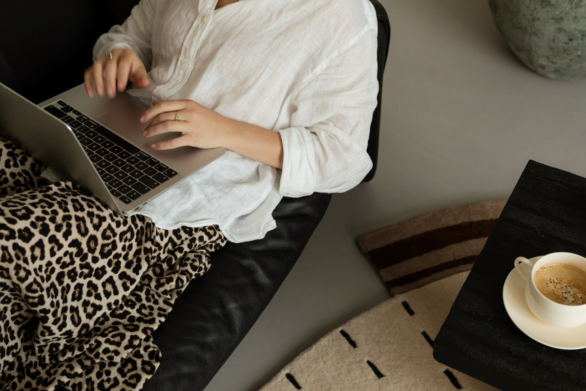 Woman working on a laptop from a black leather sofa